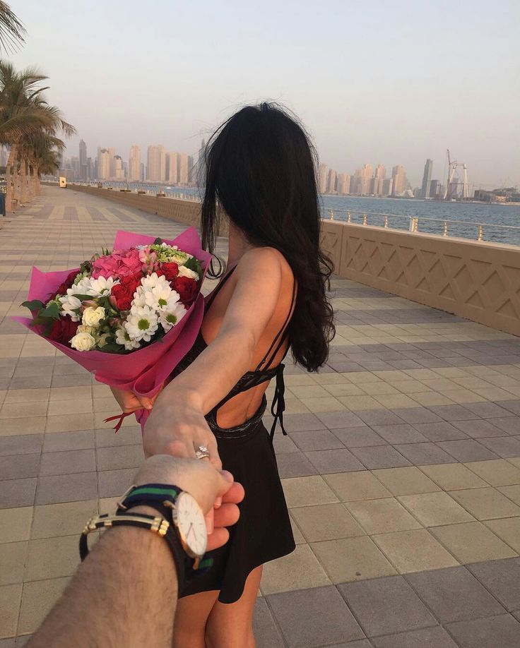 a woman holding onto a man's hand while standing on a sidewalk next to the ocean