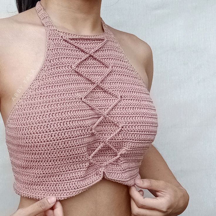 a woman wearing a pink crochet halter top and holding her hand on her hip