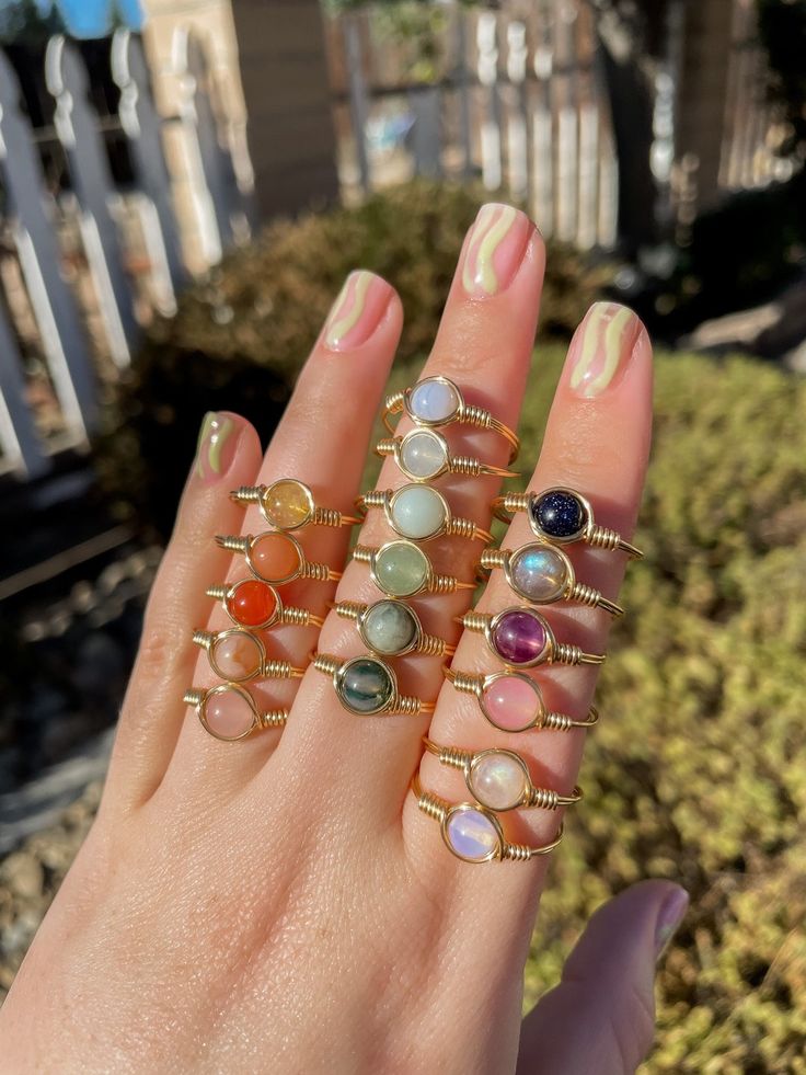 a woman's hand holding seven rings with different colored stones on them, all in gold