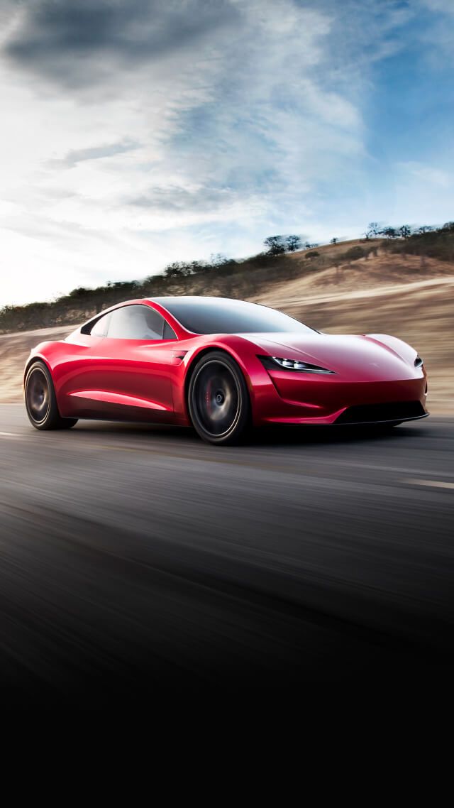 a red sports car driving down the road with clouds in the sky behind it,