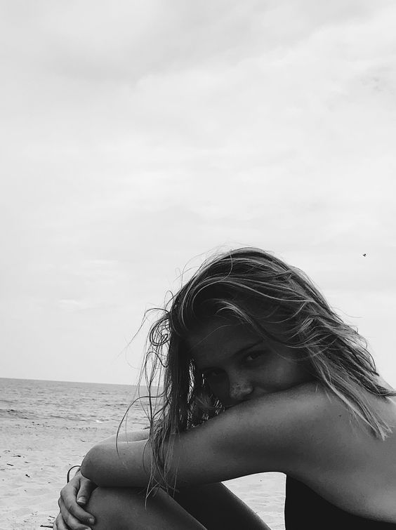 black and white photograph of a woman sitting on the beach with her hair blowing in the wind