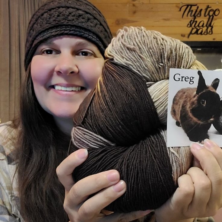 a woman holding up a ball of yarn with an animal on it and a sign that says grey