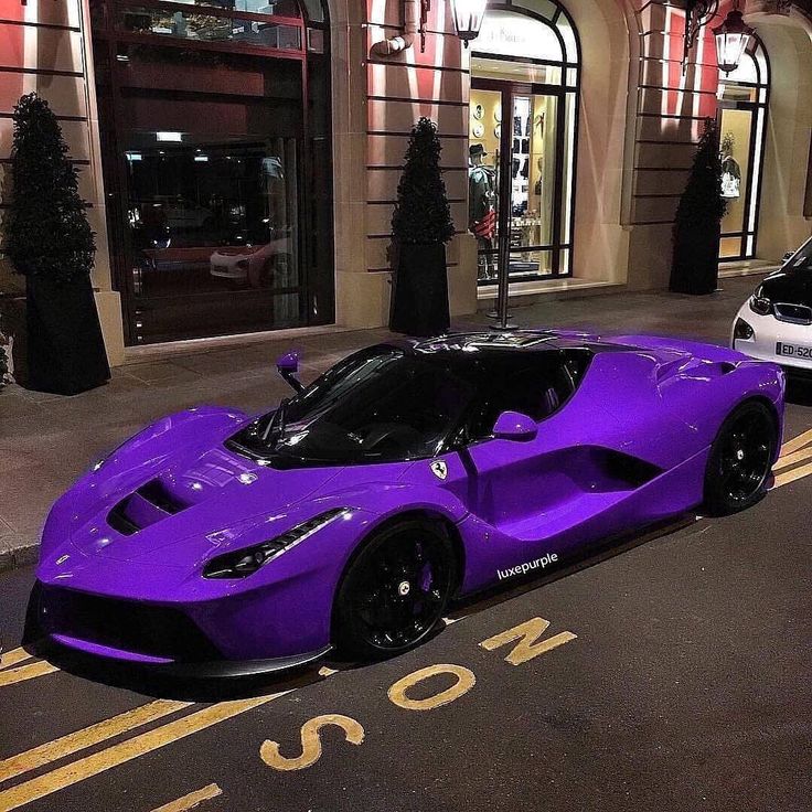 a purple sports car parked on the street in front of a building at night time