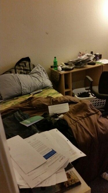 an unmade bed in a messy room with papers on the floor next to it