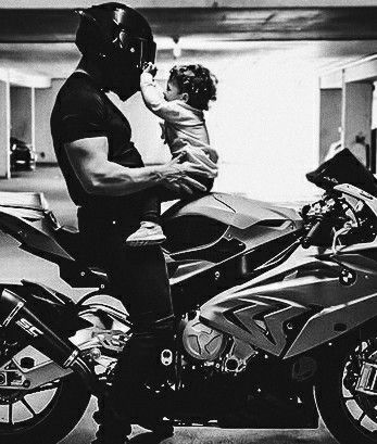 a man is holding a baby while sitting on a motorbike in a parking garage