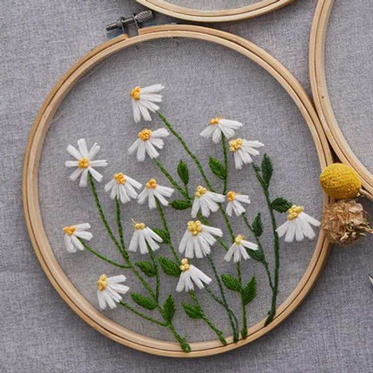 two embroidery hoops with white daisies and green leaves in them on a gray surface
