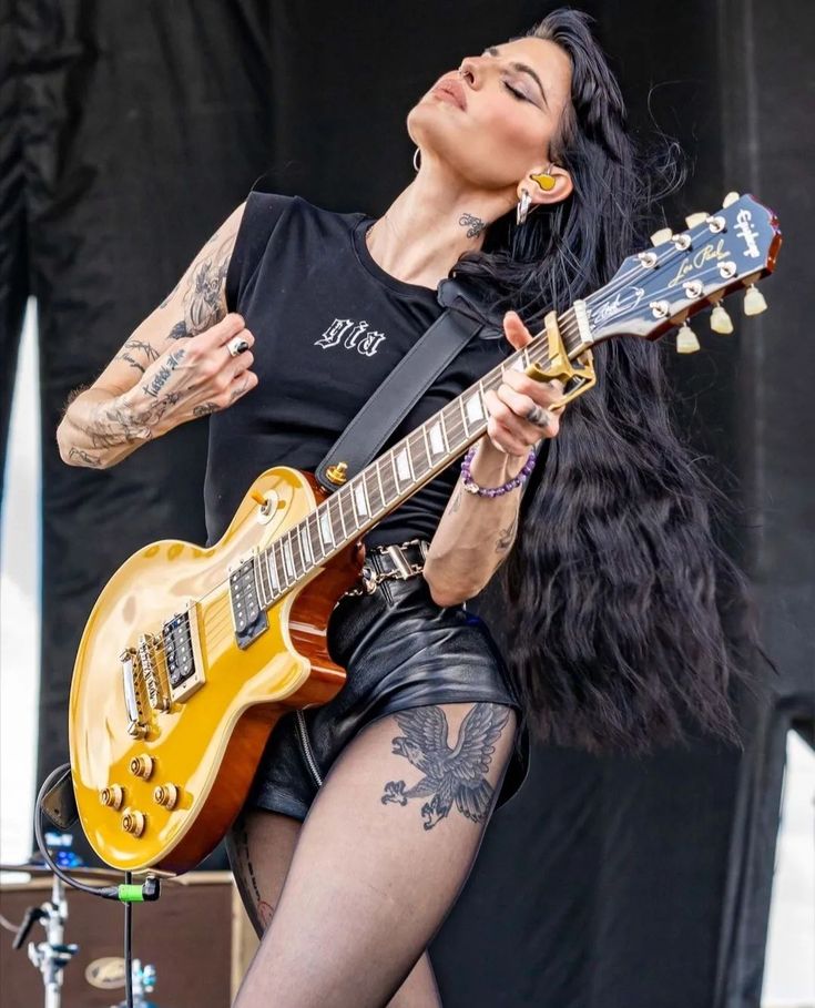 a woman with tattoos on her arm playing an electric guitar