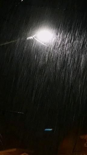 there is a street light that is shining in the rain at night with it's lights on