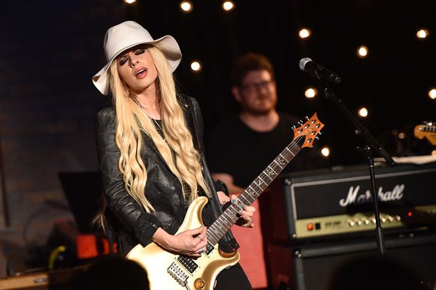 lady with long blonde hair playing guitar in front of microphone and man wearing white hat