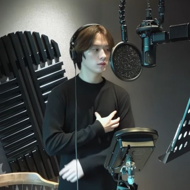 a young man wearing headphones standing in front of a microphone with his hands folded