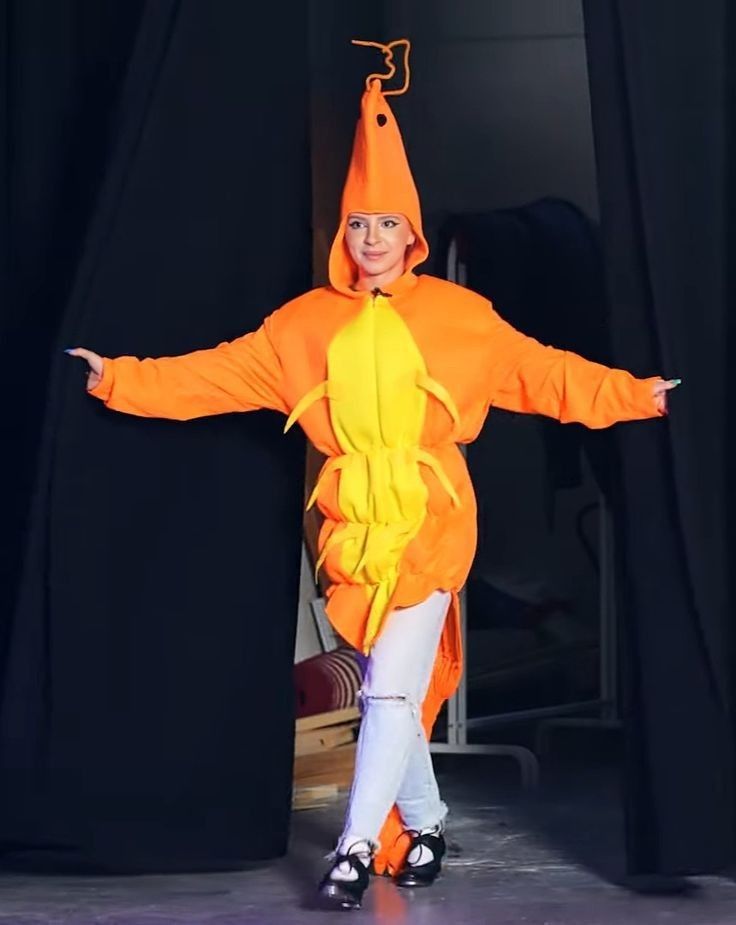 a child in an orange costume standing on stage with her arms out and hands outstretched