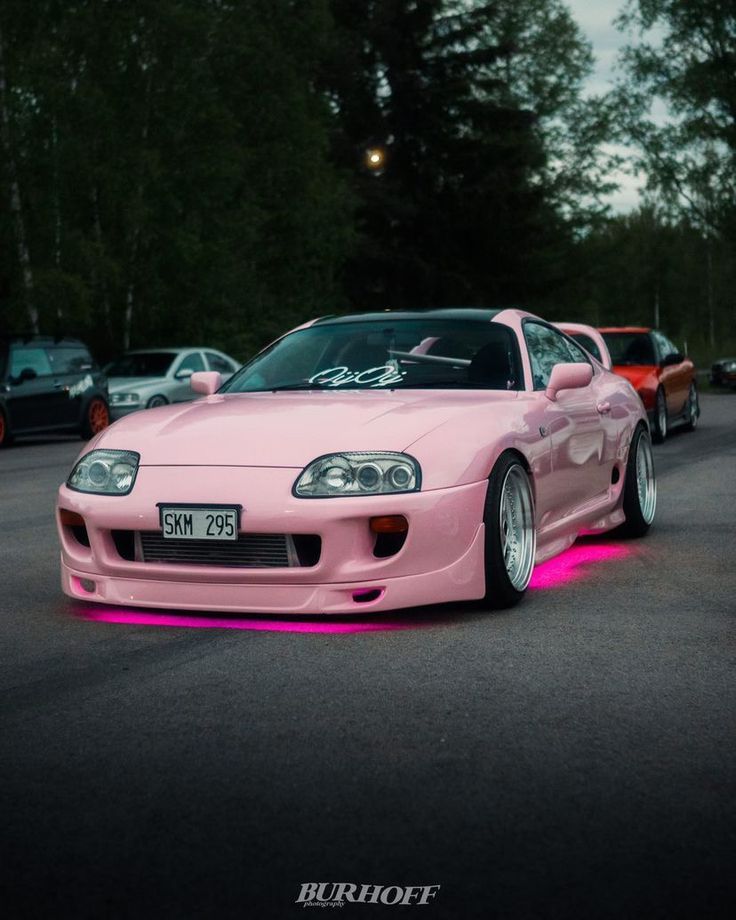 a pink sports car parked in a parking lot next to other cars with neon lights on them
