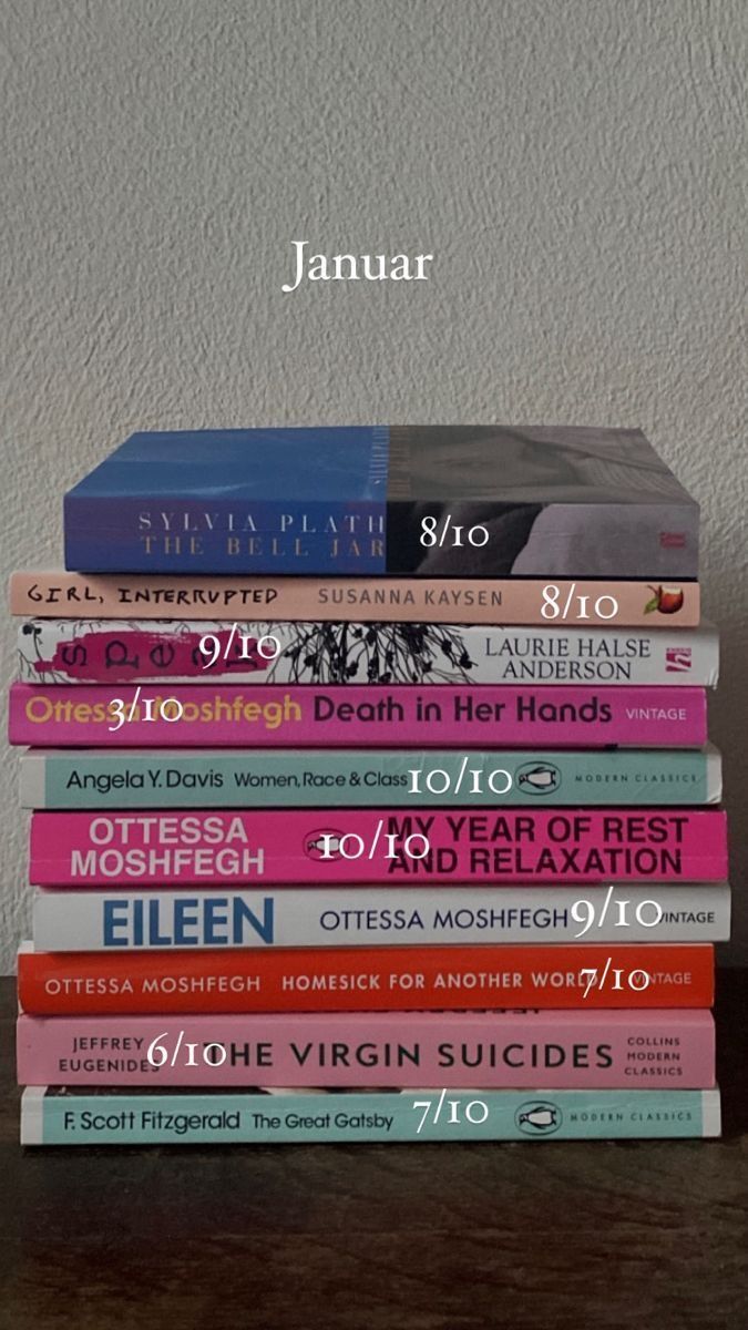 a stack of books sitting on top of a wooden table next to a white wall