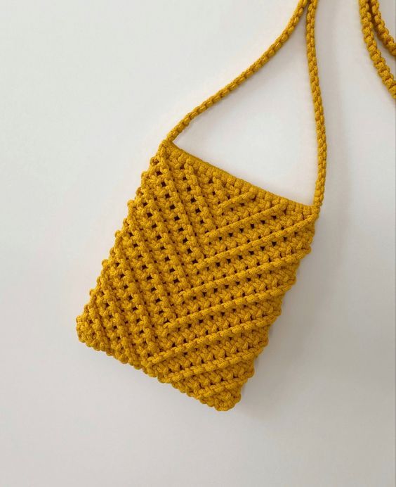 a yellow crocheted purse hanging on a white wall