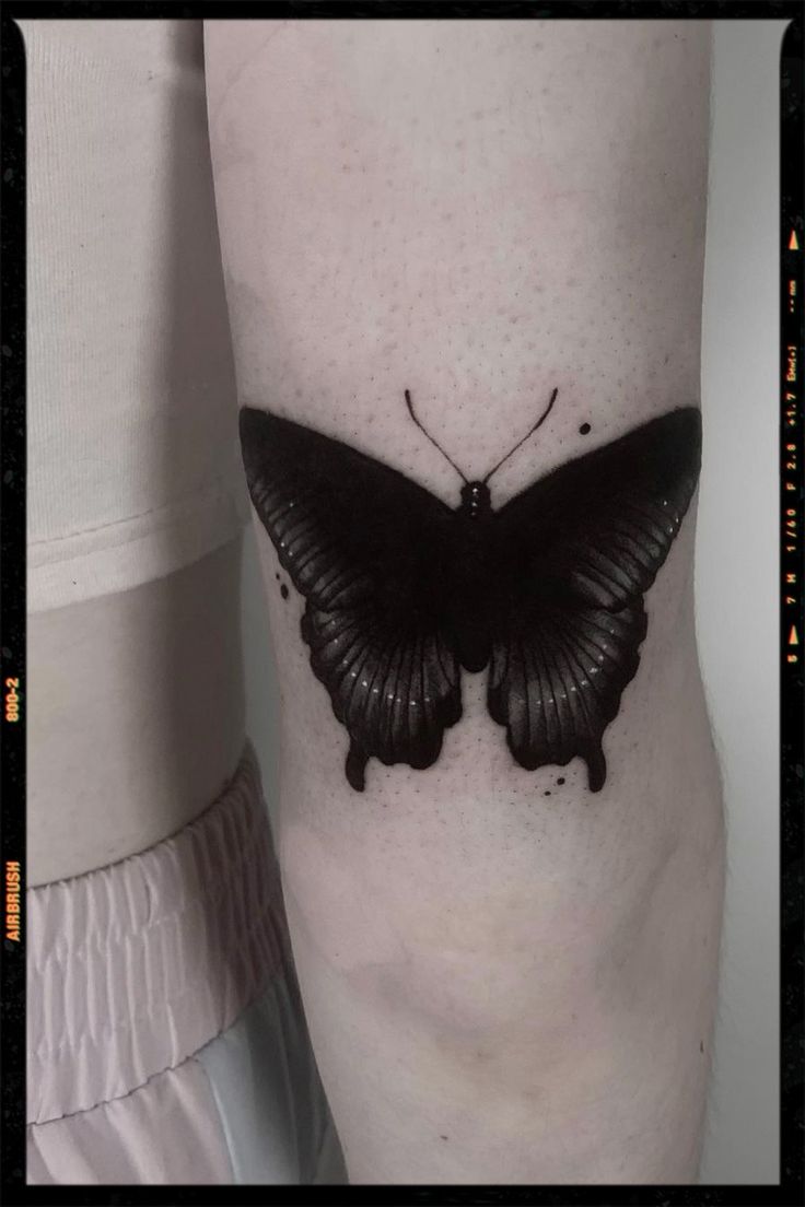 a black butterfly tattoo on the leg