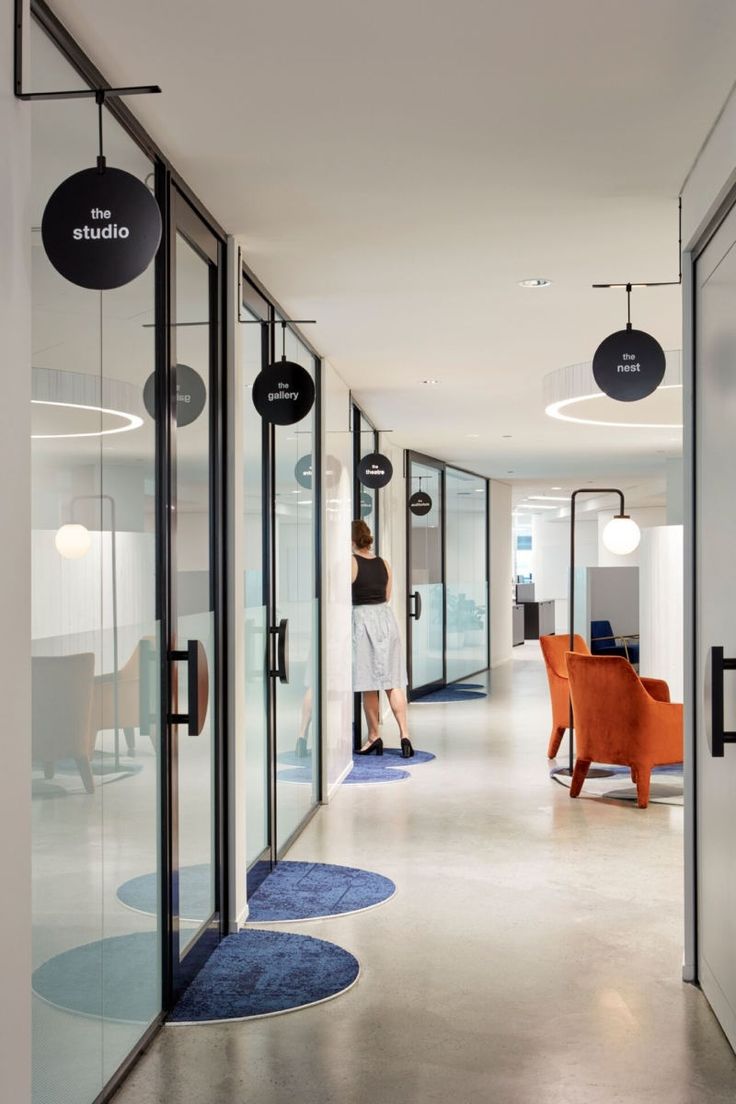 an office hallway with glass walls and hanging circles on the ceiling, two people are standing in the doorway