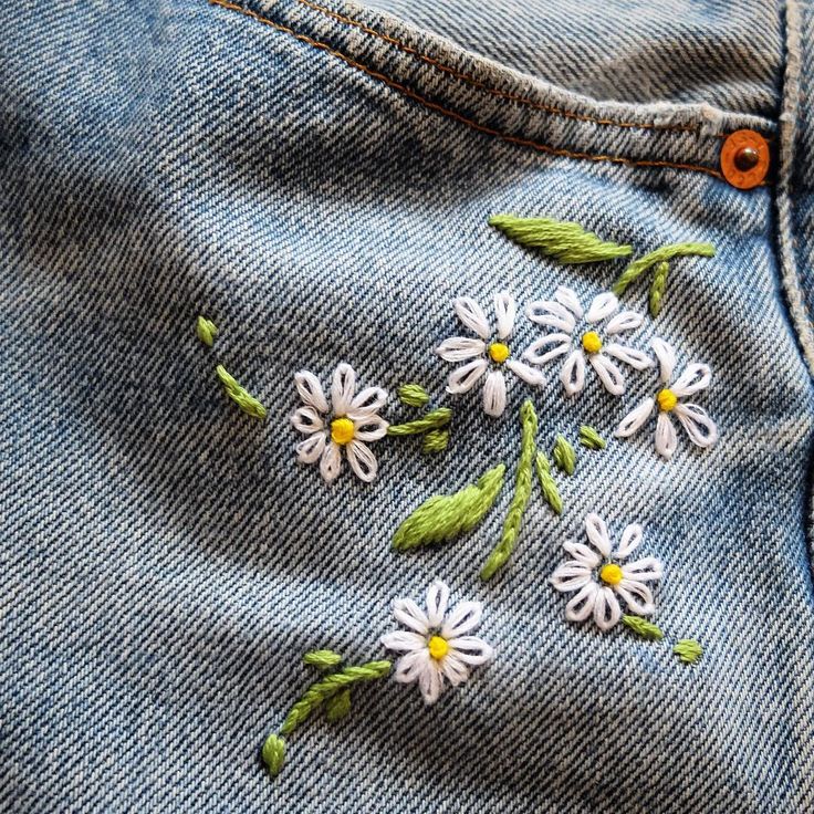 some white flowers are on the back of someone's jean pants and they look like they have been stitched together