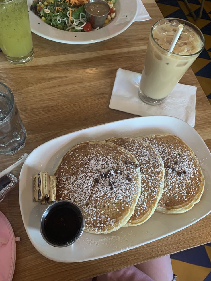 three pancakes on a white plate with powdered sugar and chocolate syrup in front of them