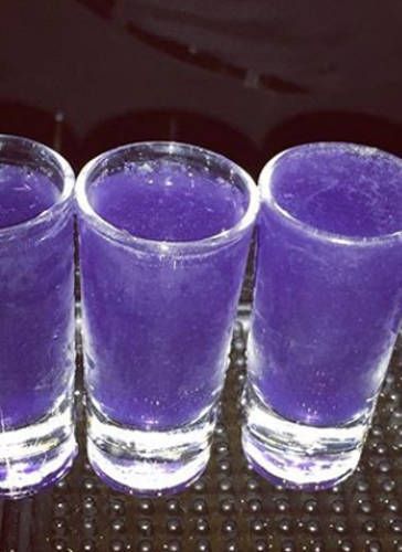 four glasses sitting on top of a table next to each other with purple liquid in them