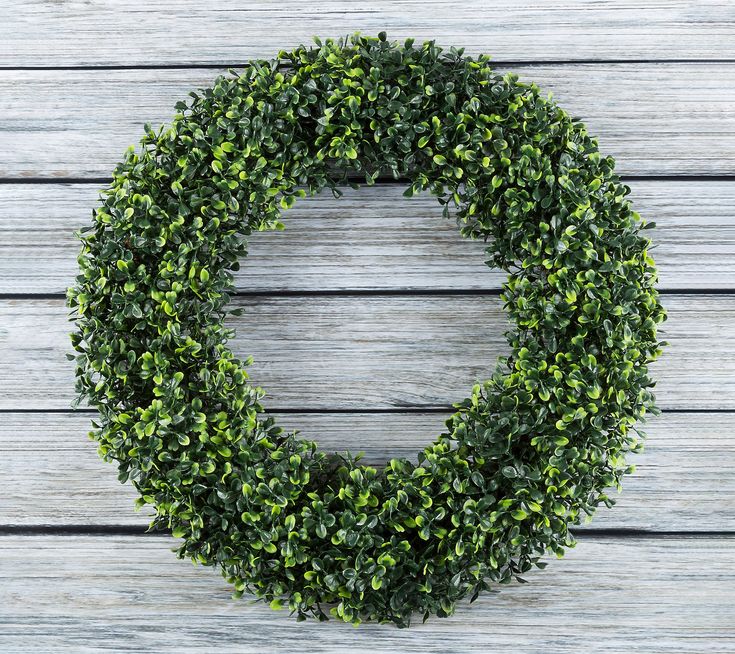 a green wreath sitting on top of a wooden table next to a white wall with wood planks