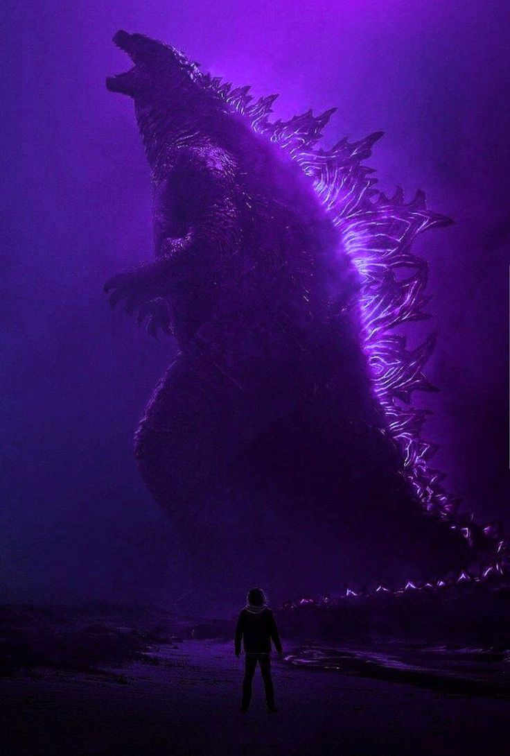 a man standing in front of a giant godzilla on the beach with purple light behind him