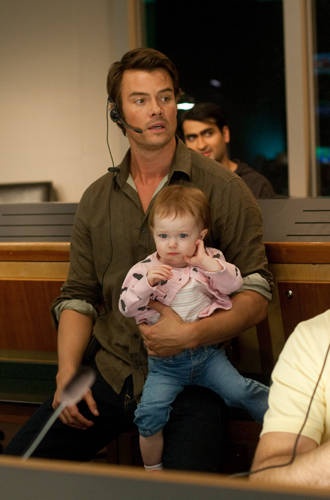 a man holding a baby in his arms while listening to headphones with other people behind him