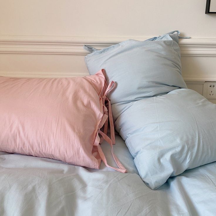 two light blue pillows on top of a bed with white sheets and pink pillow cases