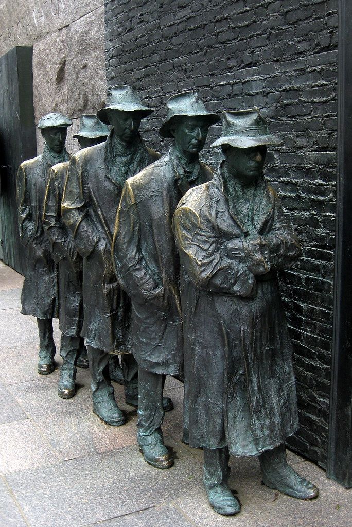 four bronze statues of men standing next to each other in front of a brick wall