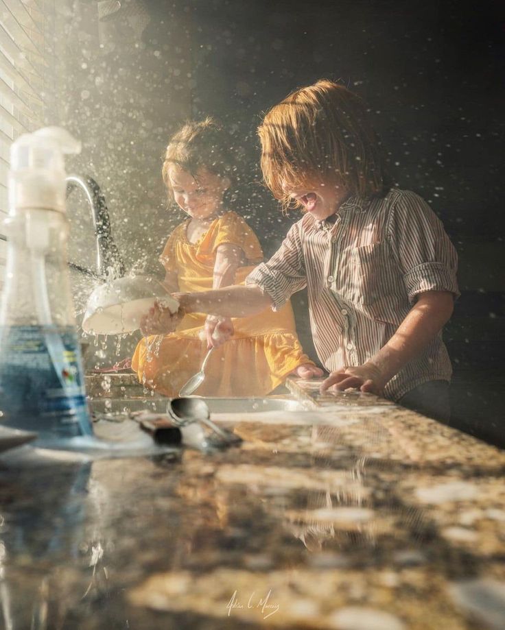 two children are washing their hands in the kitchen sink with water coming from the faucet