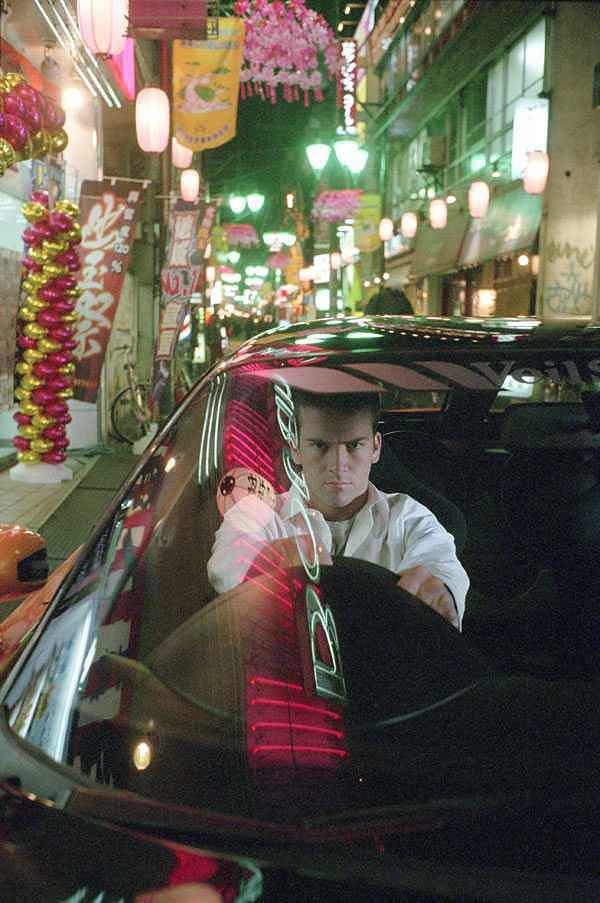 a man sitting in the driver's seat of a car on a city street at night