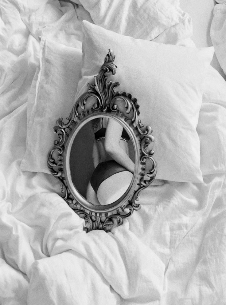 a woman's reflection in a mirror on top of a bed with white sheets