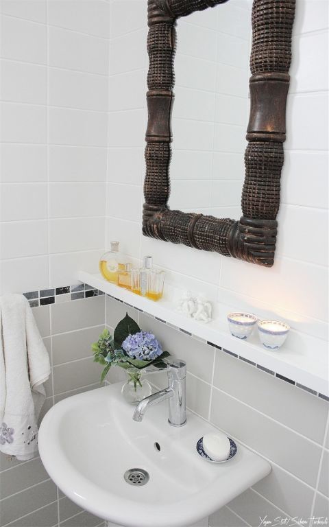 a white sink sitting under a bathroom mirror next to a shelf with soap and flowers