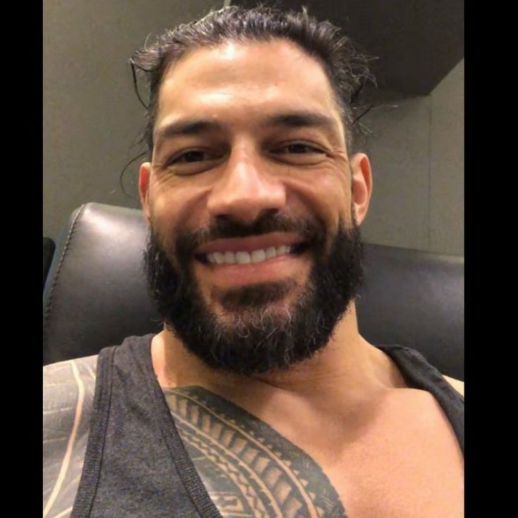 a close up of a person with a beard wearing a tank top and smiling at the camera