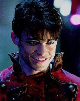 a close up of a person wearing a jacket and smiling at the camera with lights in the background