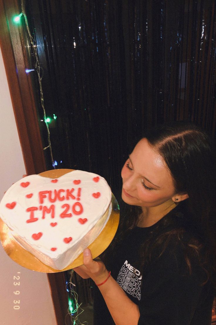 a woman holding a heart shaped cake with the words i'm 20 on it