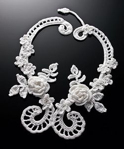a white necklace with flowers and leaves is shown on a black background in this image