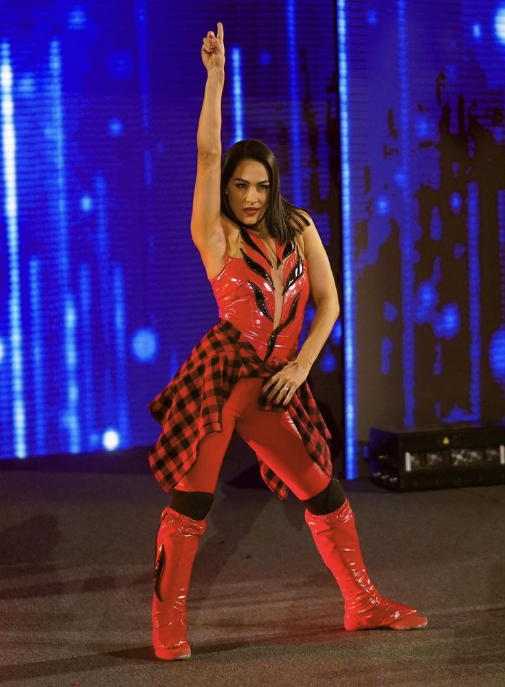 a woman dressed in red and black dancing on stage with her hand up to the sky