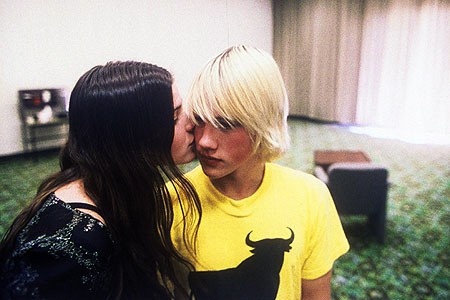 two young women kissing each other in a room with green carpeted walls and flooring