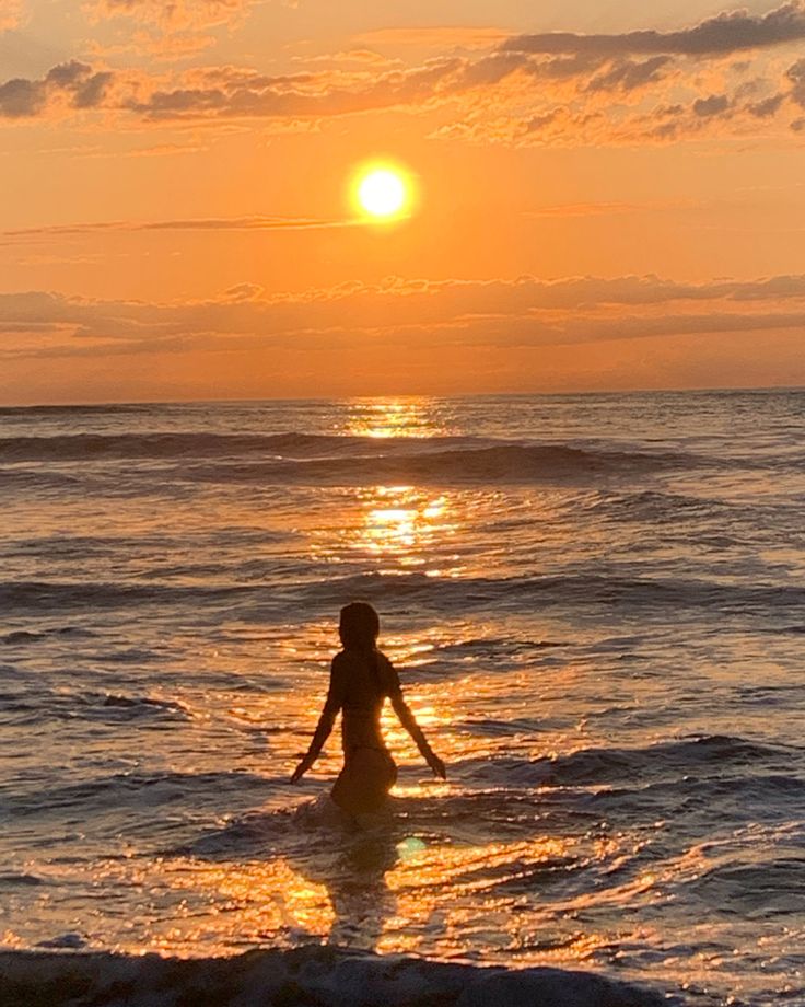 a person wading in the ocean at sunset