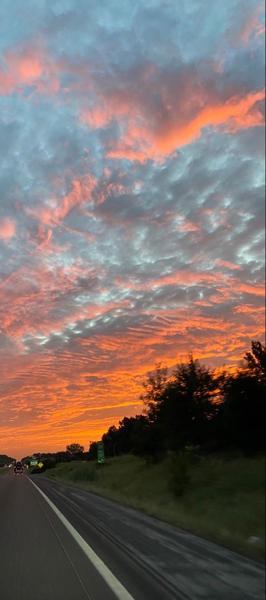 the sun is setting on an empty highway with trees in the distance and clouds in the sky