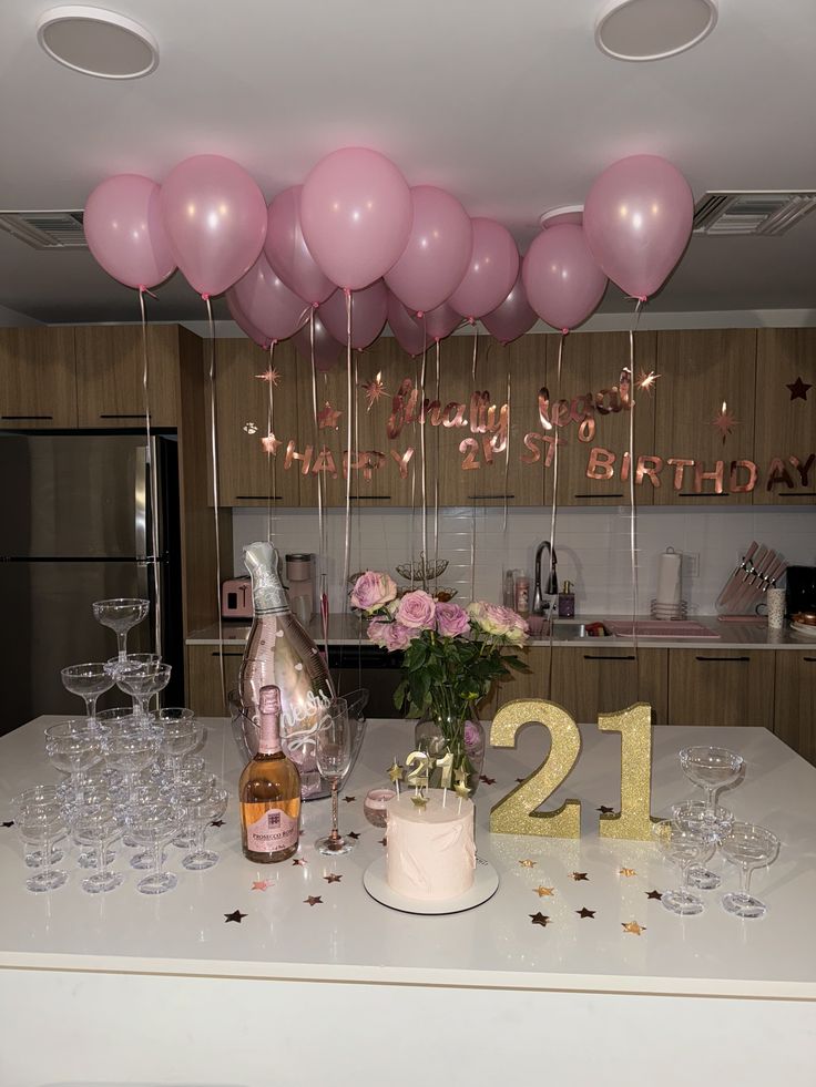 a table topped with champagne glasses and balloons next to a number twenty cake on top of a counter