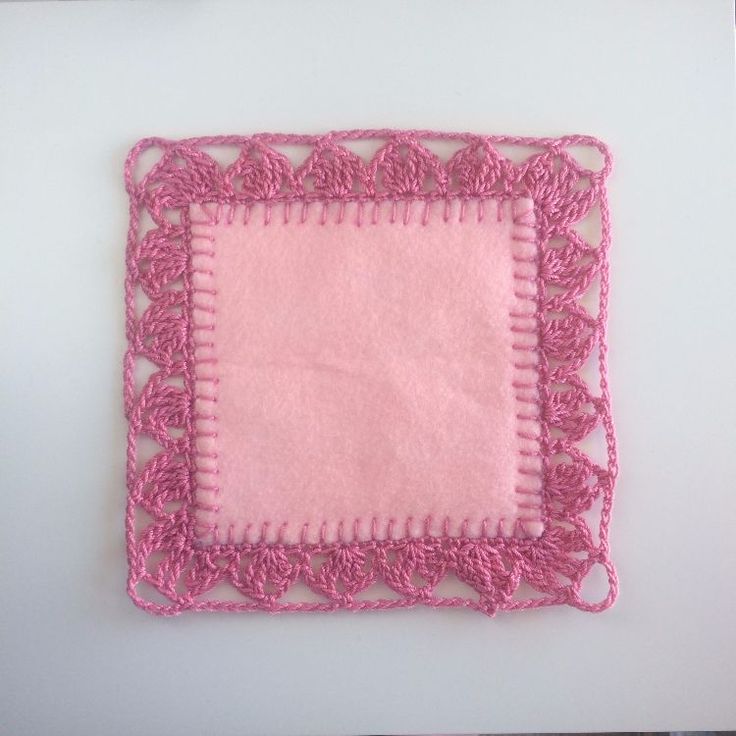 a pink square with crocheted edges on a white surface