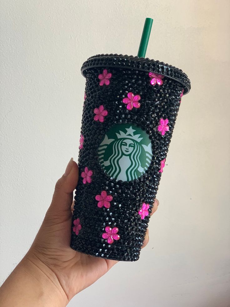 a hand holding up a black starbucks cup with pink flowers and a green straw in it