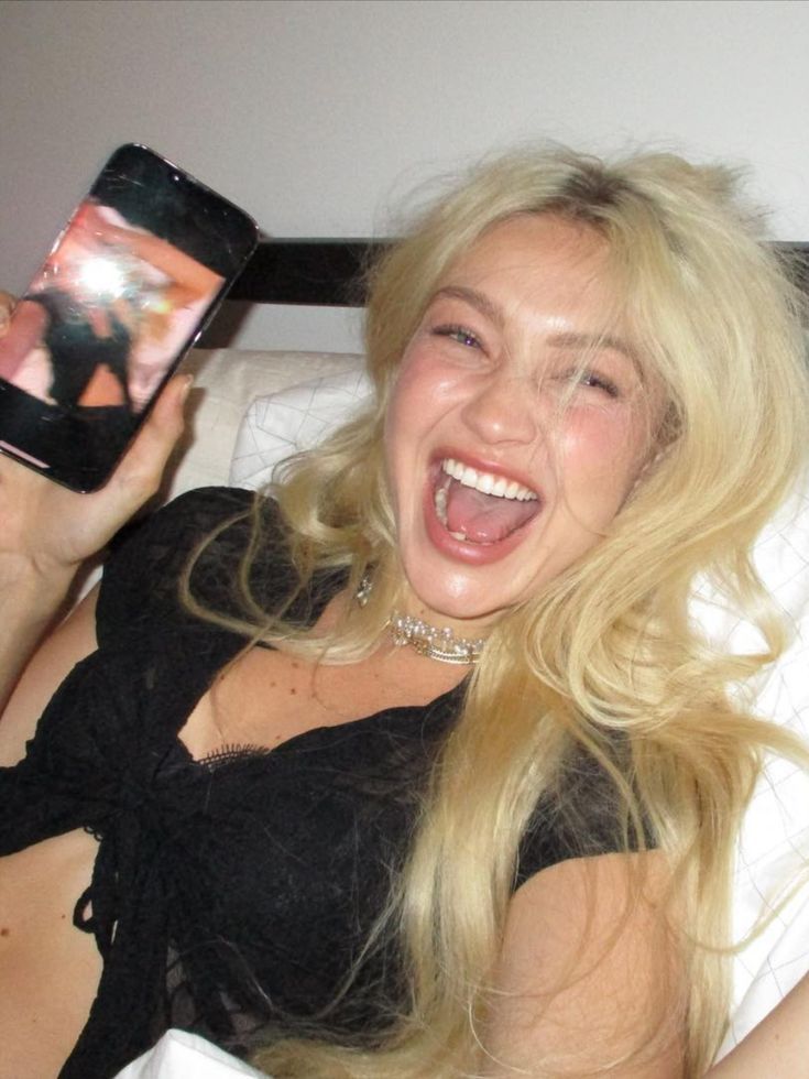 a woman laying in bed holding up a cell phone to take a selfie with her mouth open