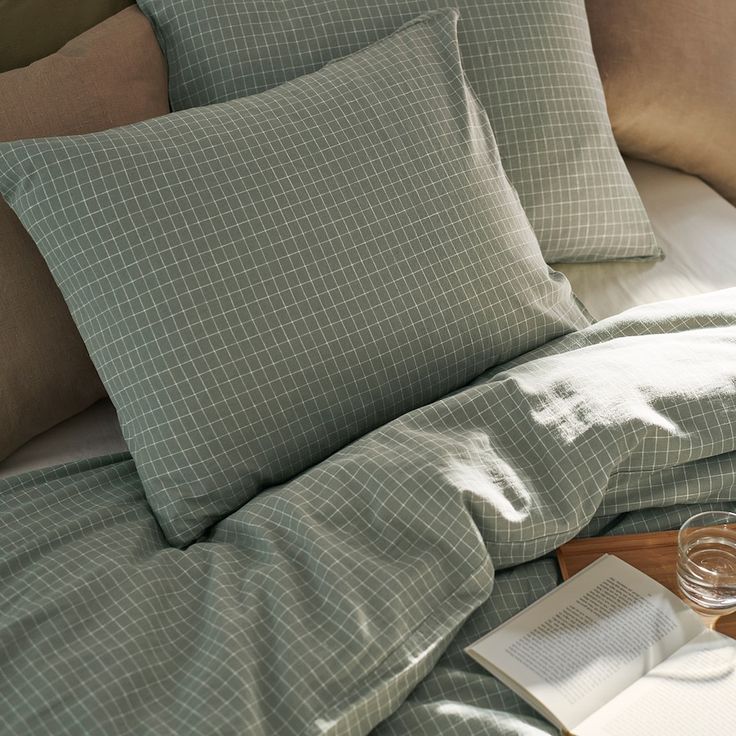 a bed with two pillows and a book on top of it next to a glass of wine