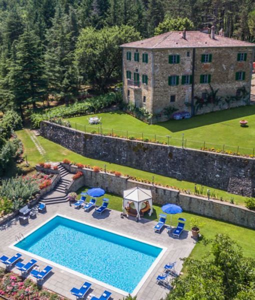 an aerial view of a house with a swimming pool in the foreground and lawn chairs around it