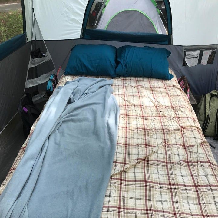 a bed in the back of a tent with blue pillows and blankets on top of it