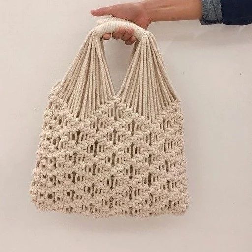 a hand holding a crocheted bag on top of a white wall