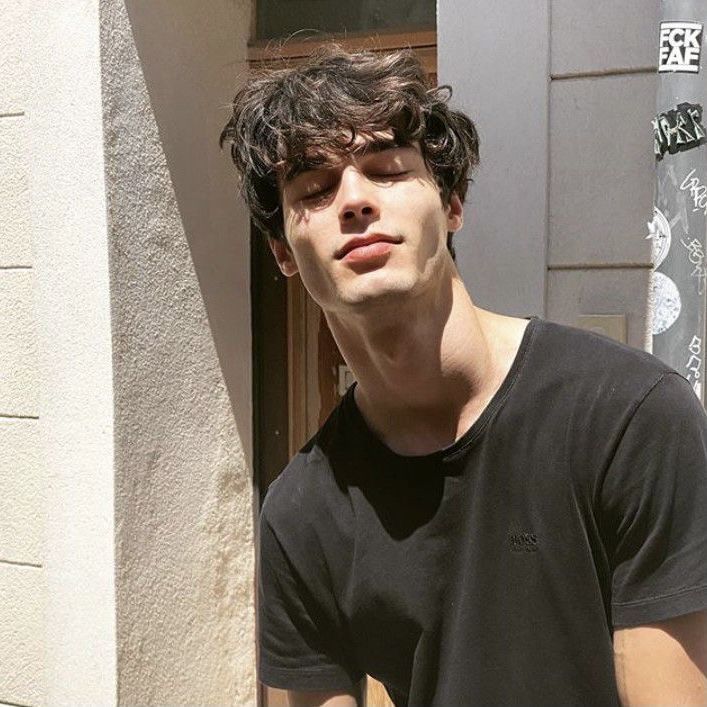 a young man standing in front of a building with his eyes closed and one hand on his hip