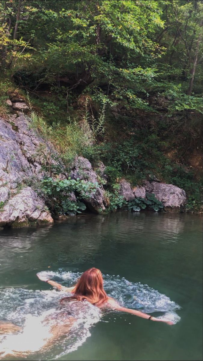 a woman laying on her back in the middle of a body of water surrounded by rocks